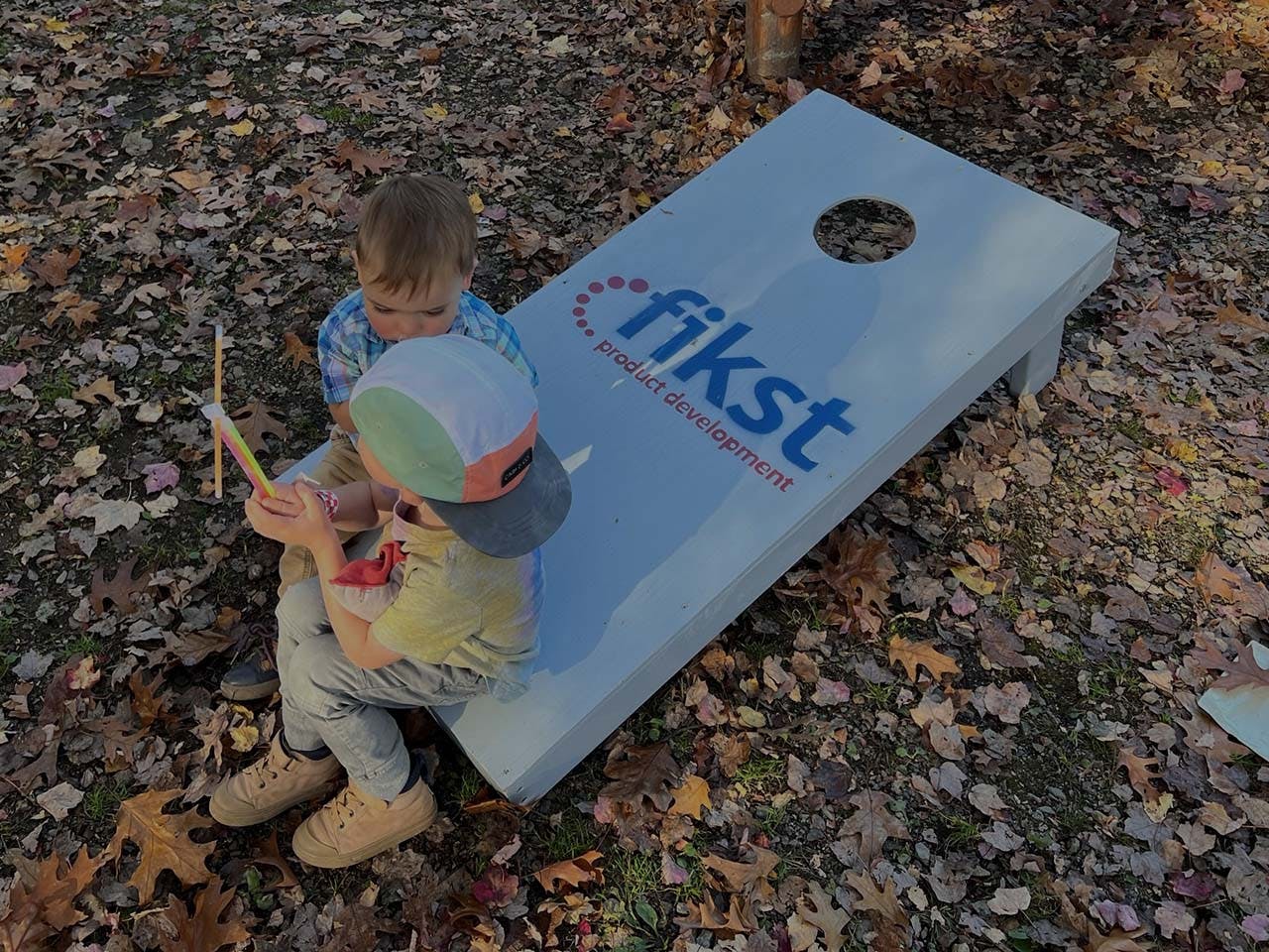 Two children sitting and playing on the edge of a Fikst corn hole game board