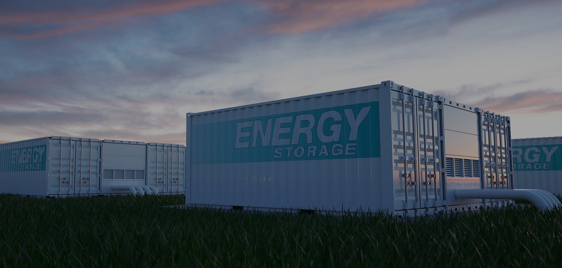 Image of battery storage containers sitting in a grassy field with a moody sunset behind .