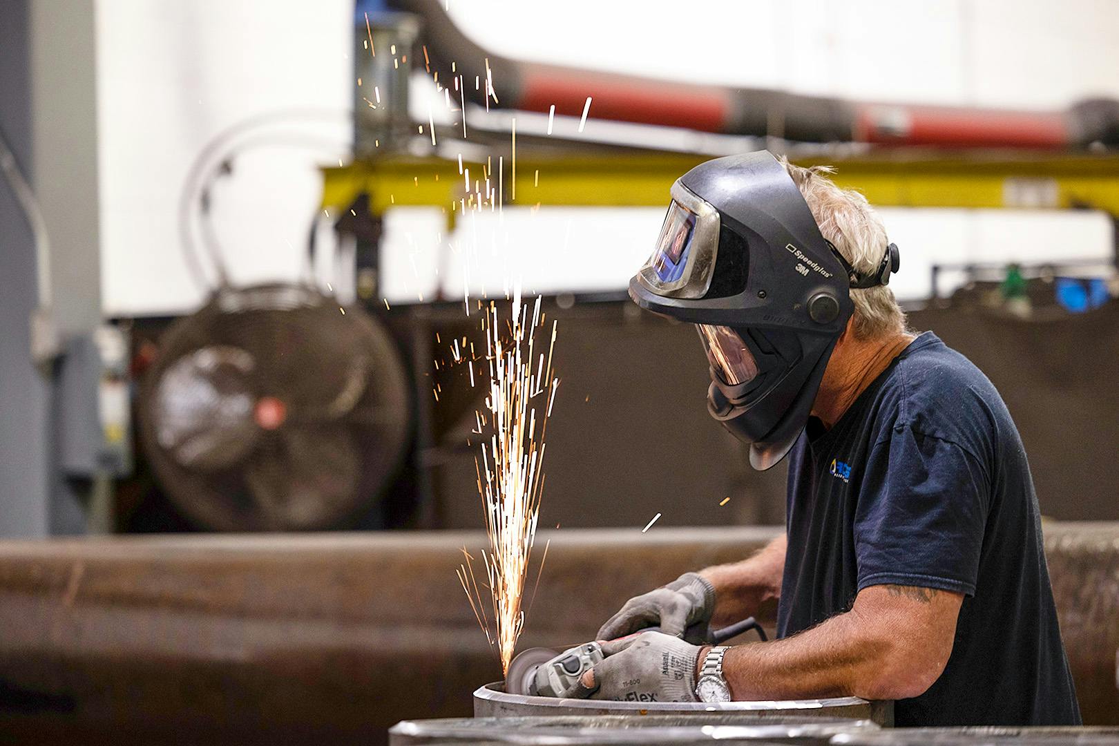 Man welding a piece of metal with sparks flying up near his face mask